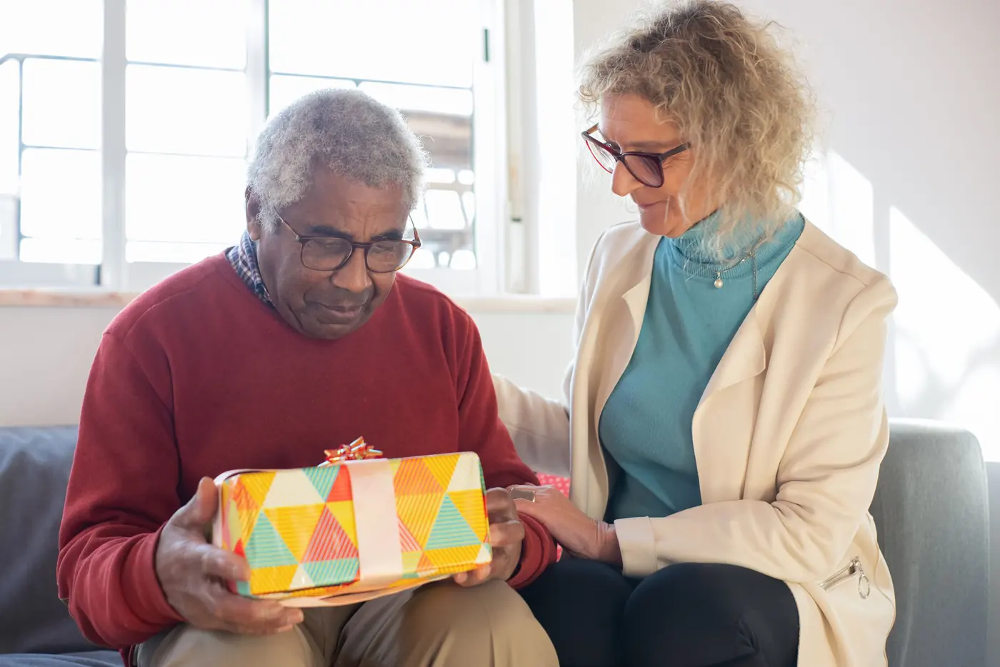 A carer sitting with an older man as he opens a gift at home