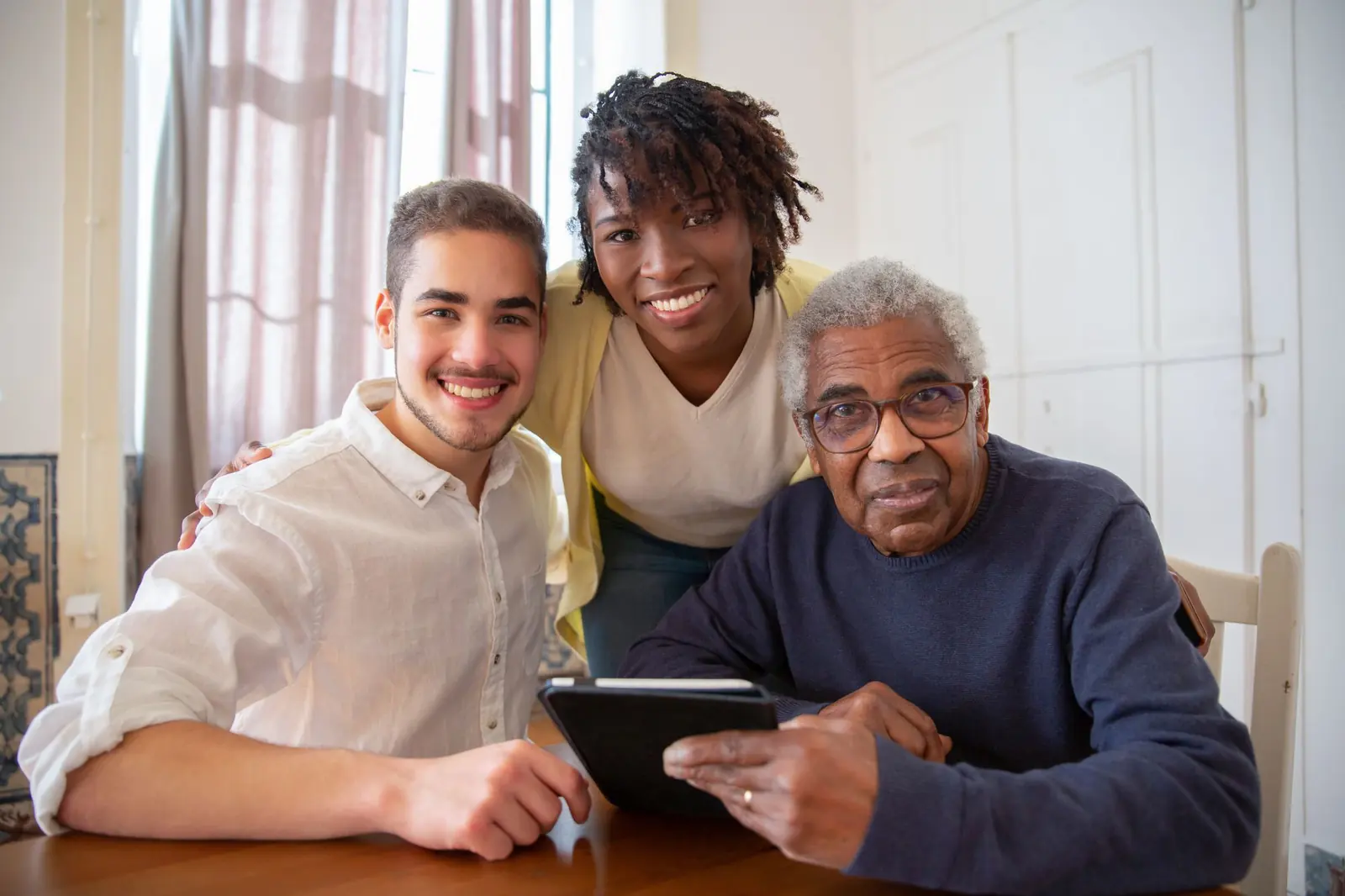 A carer and a young man smiling with an older man at his kitchen table at home