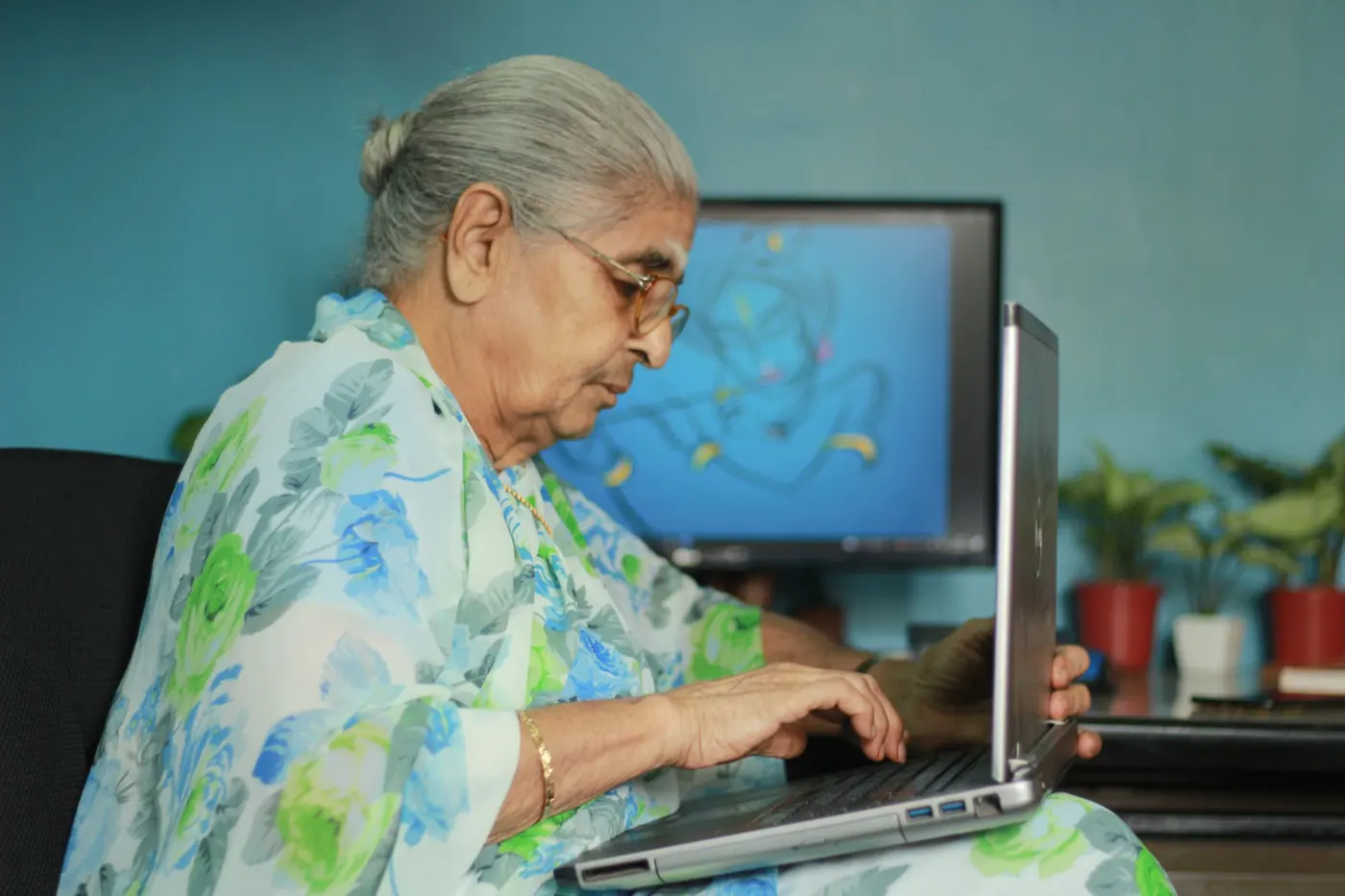 An older woman in a floral sari using a laptop at home